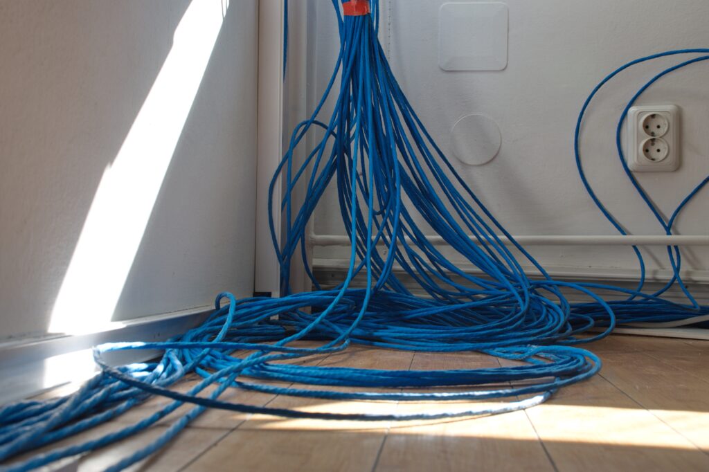Numerous blue network cables are gathered in the corner of a room, trailing along the floor near a power outlet and white walls—a scene fit for any professional guide on organizing tech spaces in [sa_city].